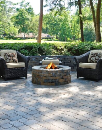 A beautiful outdoors pavers with two comfortable armchairs and a fire pit in a natural green environment