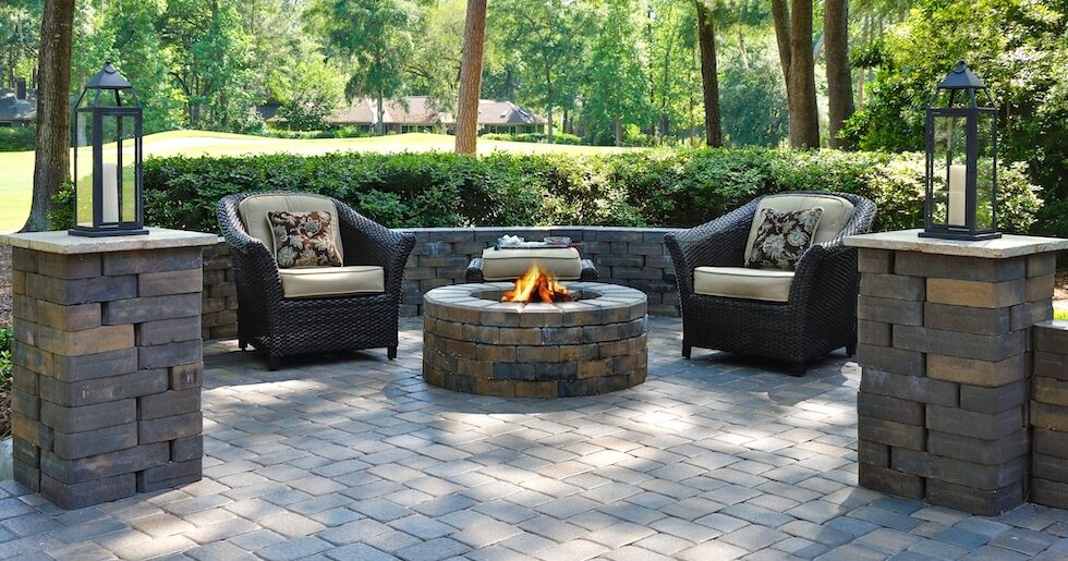 A beautiful outdoors pavers with two comfortable armchairs and a fire pit in a natural green environment